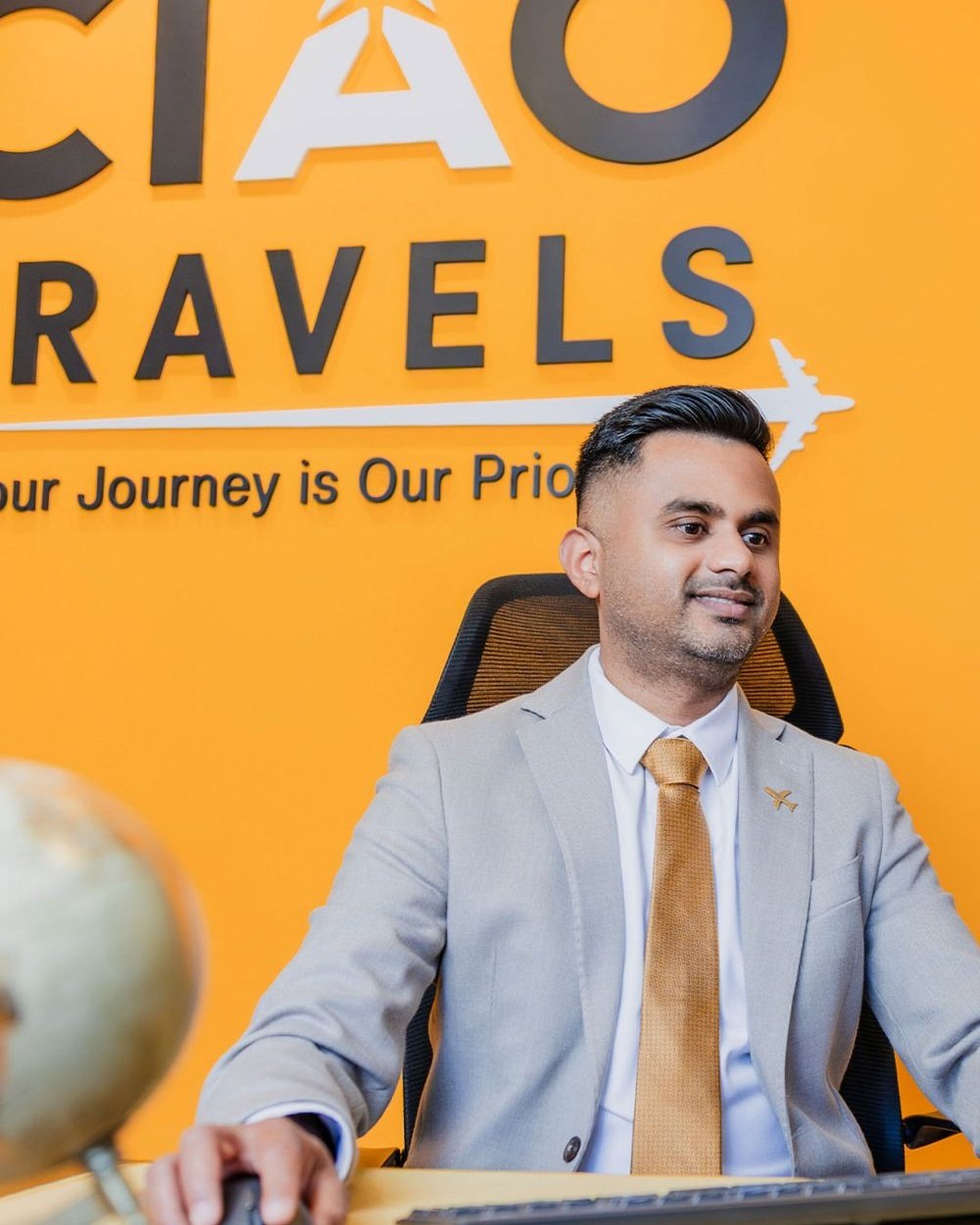 Malinga Fernando alla scrivania gialla di CIAO Travels, sotto la scritta Your Journey is Our Priority